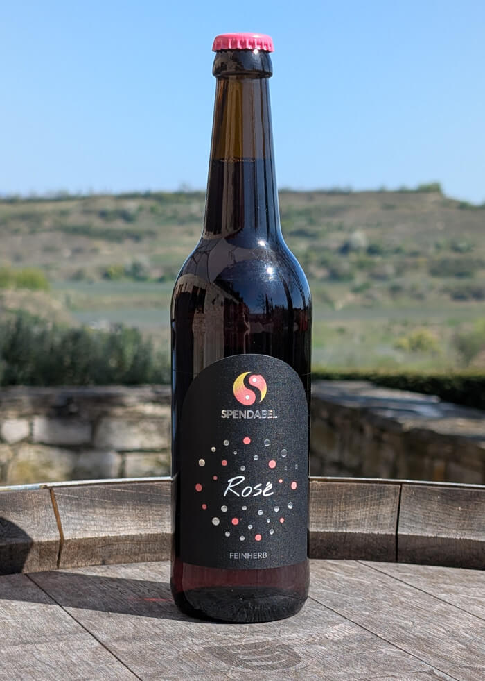 0,5 Liter Flasche SPENDABEL Rosewein Rosé feinherb auf einem Weinfass mit Weinbergen im Hintergrund