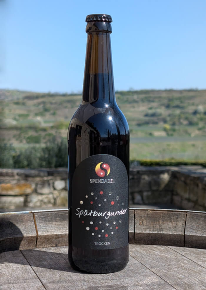 0,5 Liter Flasche SPENDABEL Rotwein Spätburgunder trocken auf einem Weinfass mit Weinbergen im Hintergrund