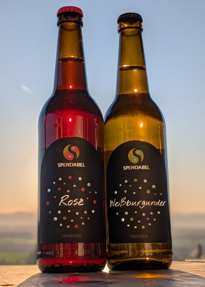 Eine Flasche SPENDABEL Rosé feinherb und eine Flasche SPENDABEL Weißburgunder trocken vor einem Sonnenuntergang